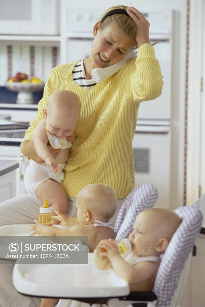 Stock Photo: 1099-1802A Mother with her three baby boys talking on a cordless phone