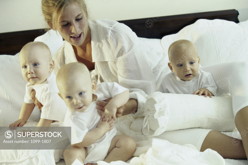 Stock Photo: 1099-1807 Mother sitting on a bed with her three baby boys