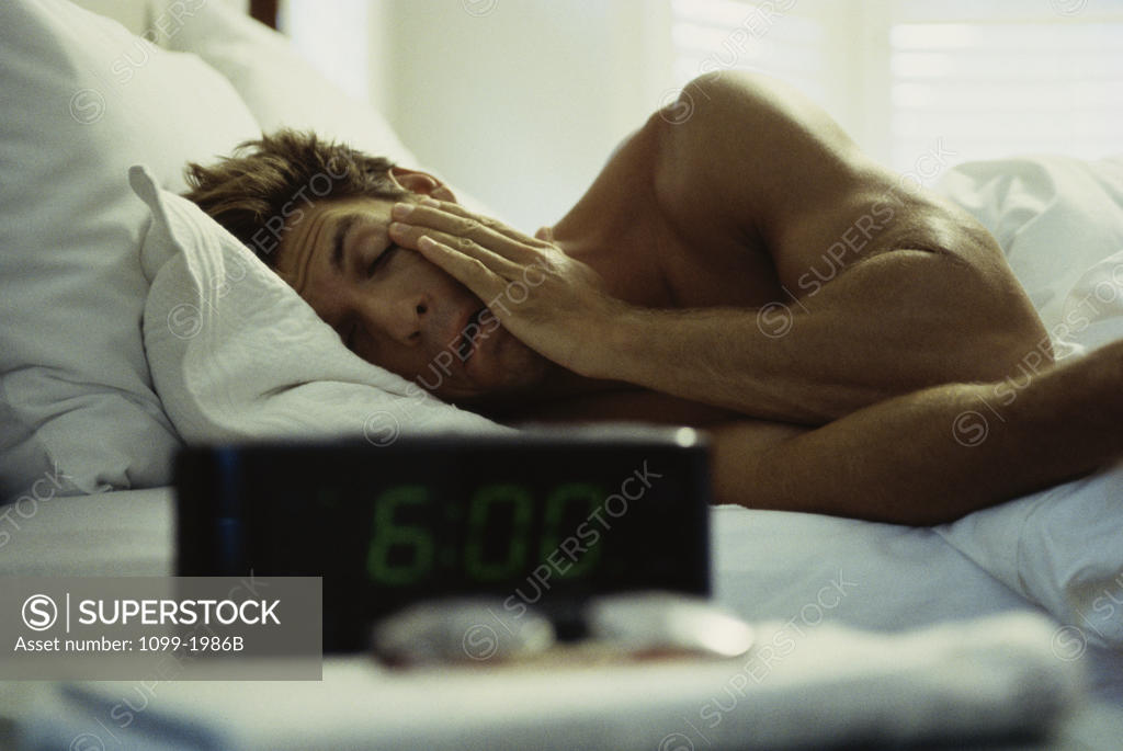Stock Photo: 1099-1986B Young man rubbing his eyes in bed