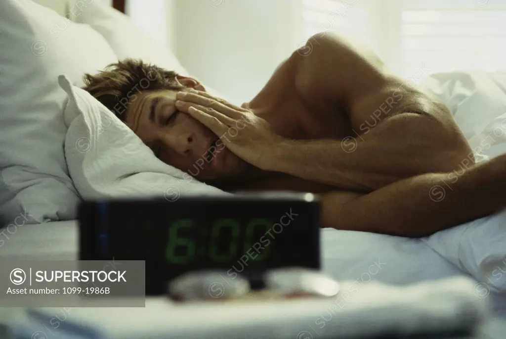 Young man rubbing his eyes in bed