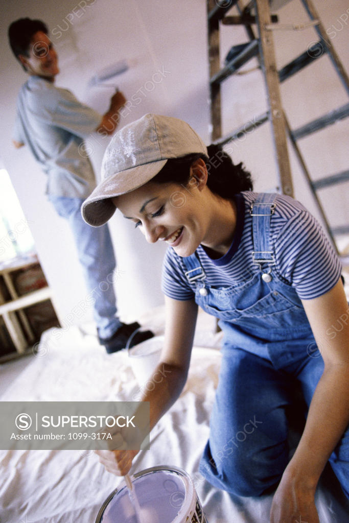 Stock Photo: 1099-317A Young woman mixing paint with a young man painting the wall behind her