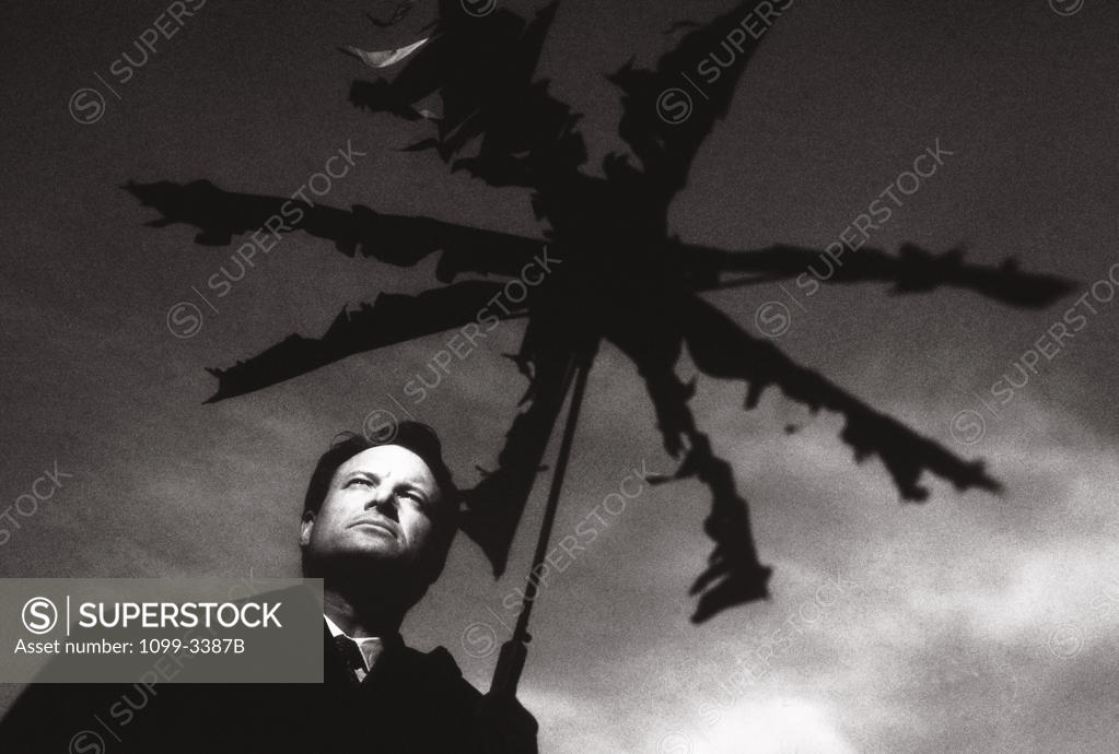 Stock Photo: 1099-3387B Low angle view of a businessman standing under a broken umbrella