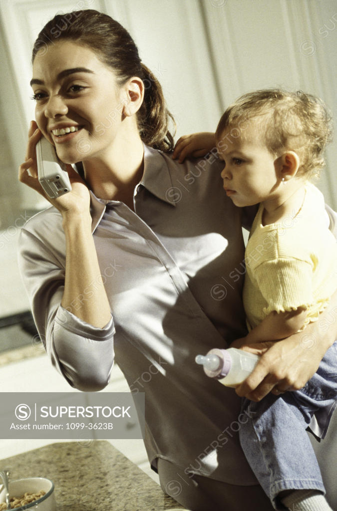 Stock Photo: 1099-3623B Babysitter carrying a baby and talking on a cordless phone