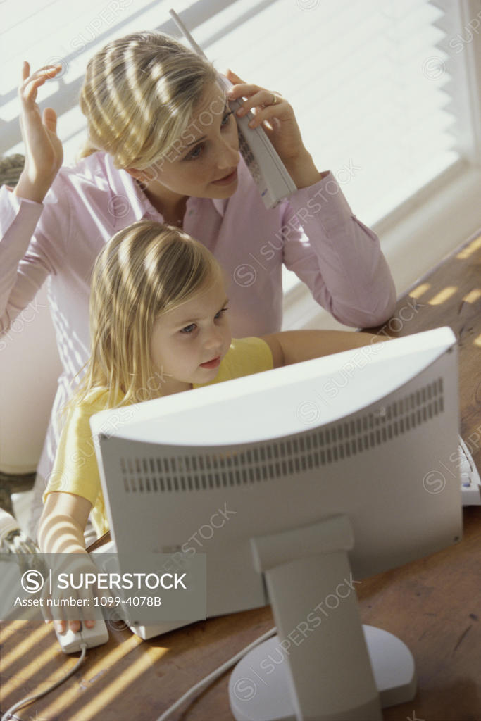 Stock Photo: 1099-4078B Young woman talking on a cordless phone and her daughter using a computer
