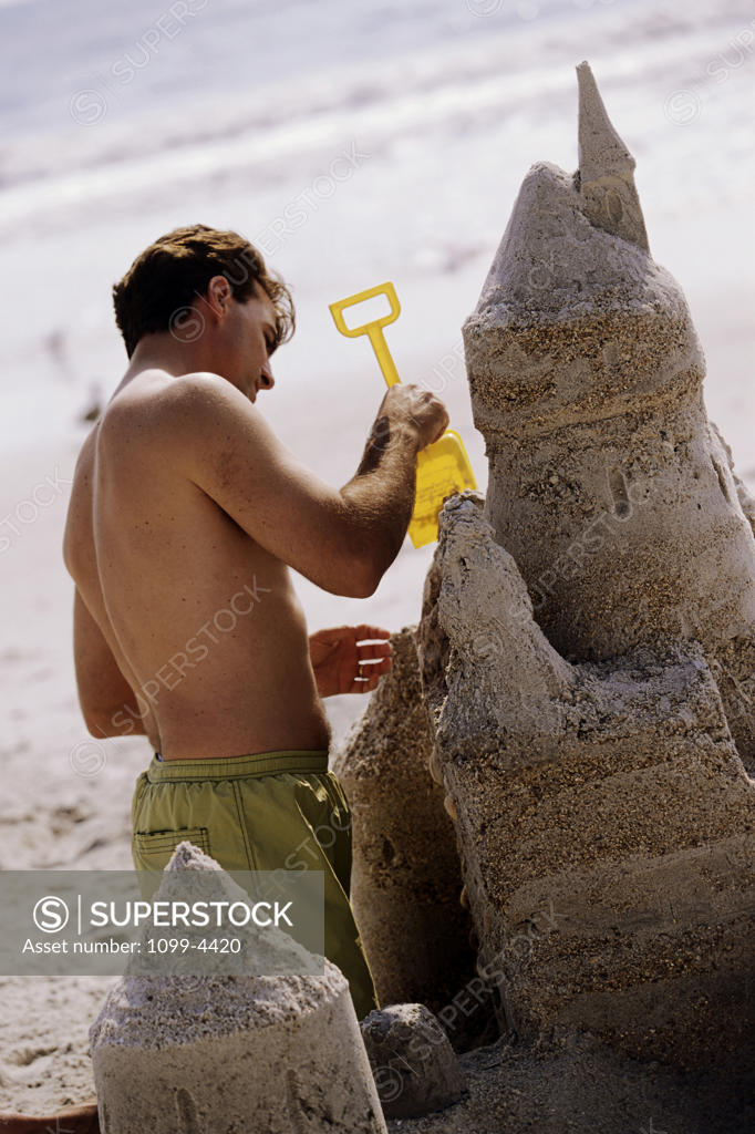 Stock Photo: 1099-4420 Rear view of a young man building a sand castle on the beach