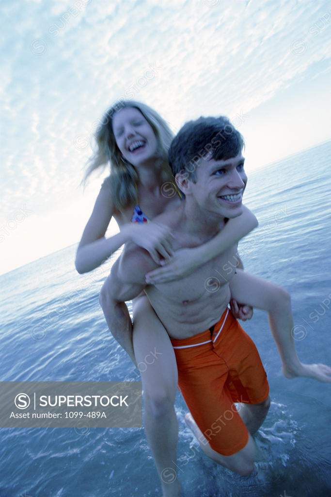 Stock Photo: 1099-489A Young woman riding piggyback on a young man on the beach