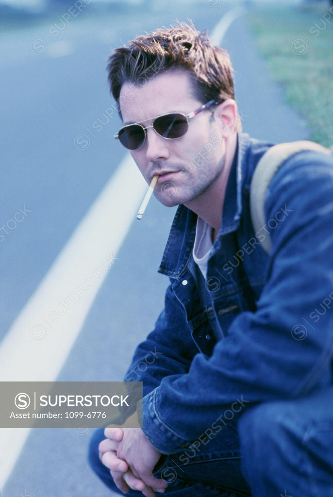 Stock Photo: 1099-6776 Side profile of a young man squatting on the road smoking a cigarette