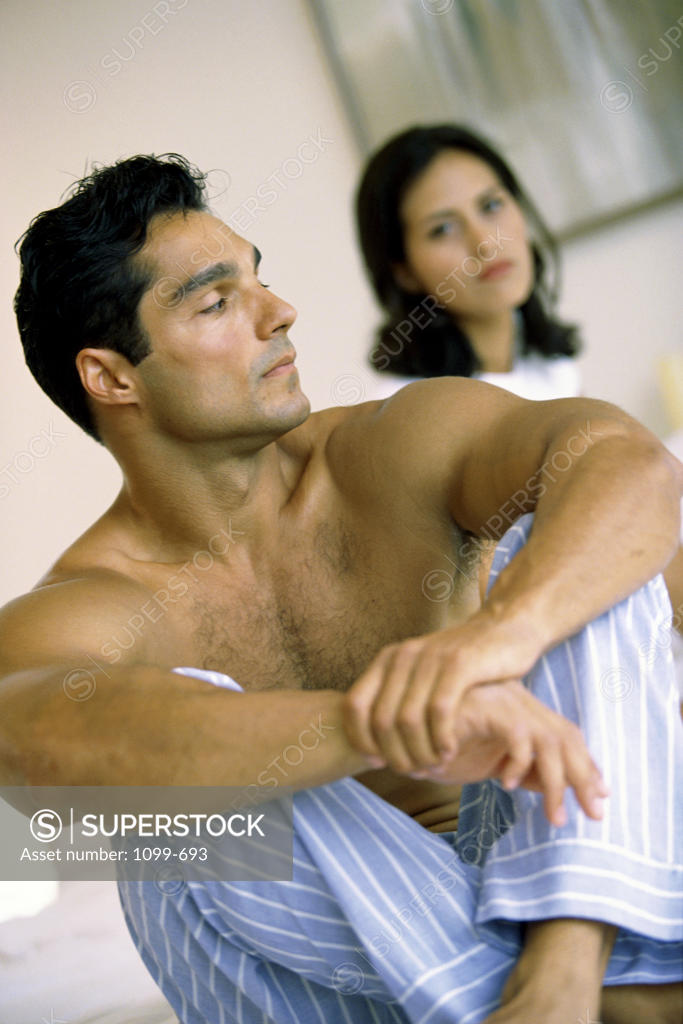 Stock Photo: 1099-693 Young man sitting on a bed with a young woman behind him
