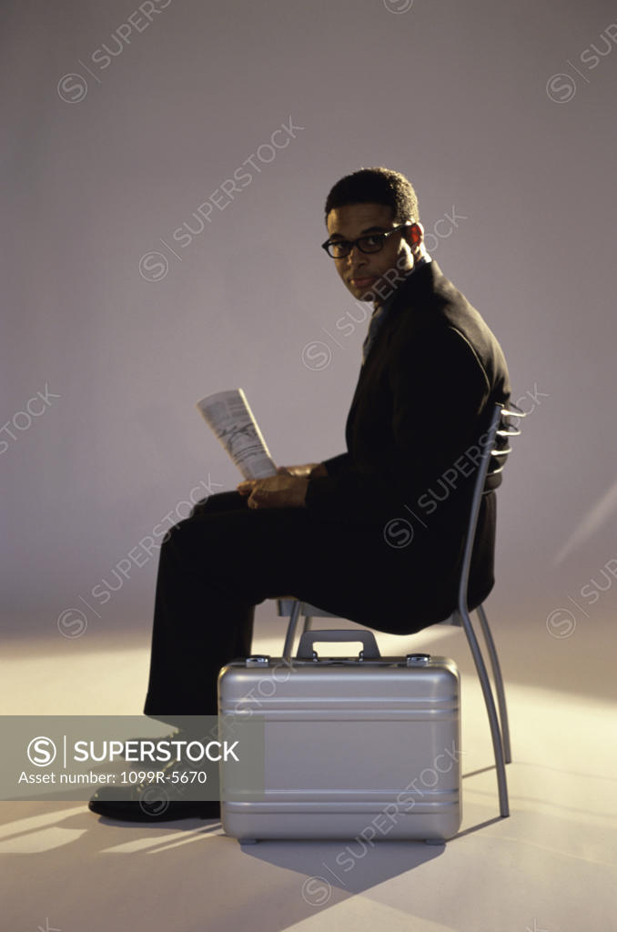 Stock Photo: 1099R-5670 Businessman sitting on a chair holding a newspaper
