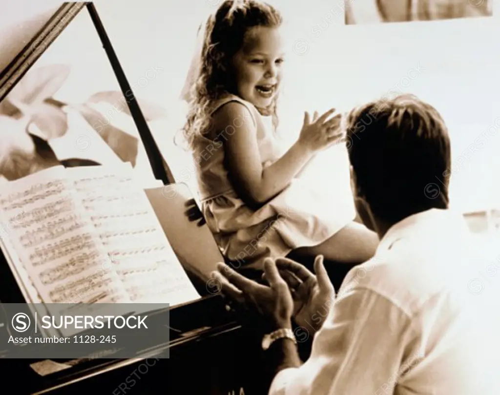 Man clapping hands sitting with a child at the piano