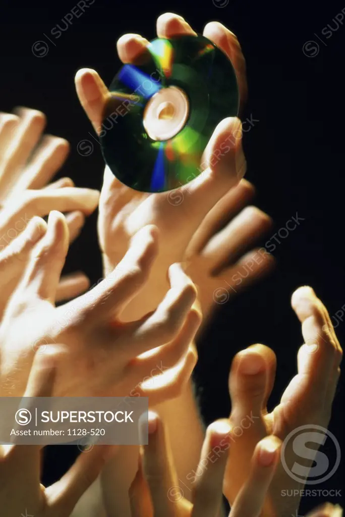 Close-up of a group of peoples hands reaching up for a compact disc