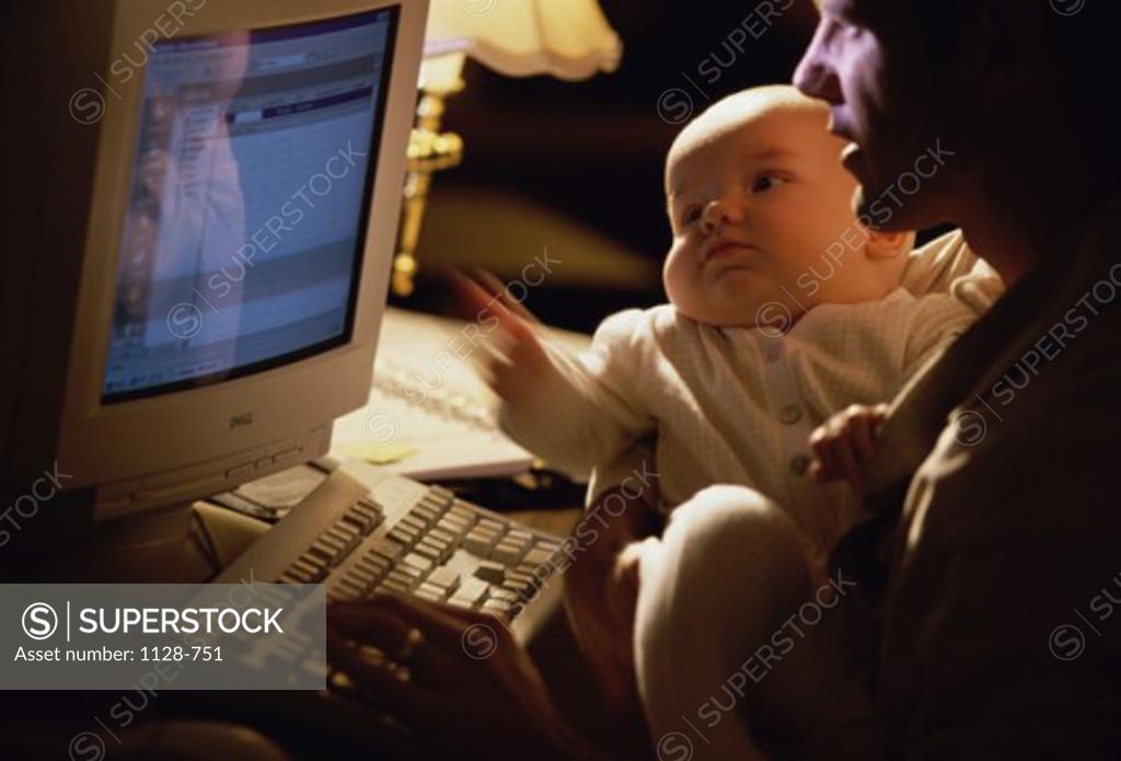 Stock Photo: 1128-751 Father holding his baby working on a computer