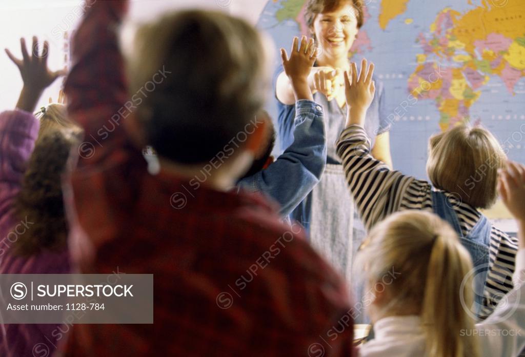 Stock Photo: 1128-784 Teacher standing in front of a classroom with her students raising their hands