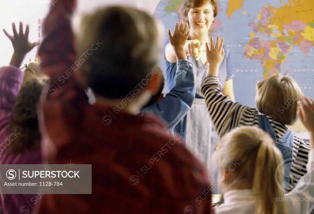 Teacher standing in front of a classroom with her students raising their hands