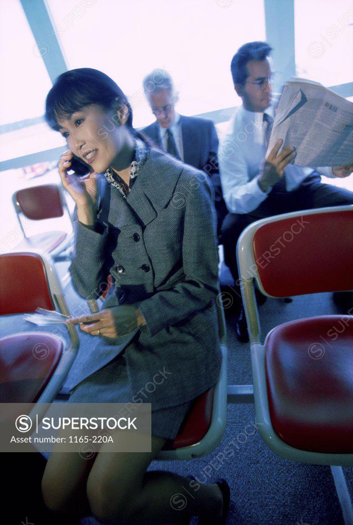 Stock Photo: 1165-220A Businesswoman talking on a mobile phone sitting in front of two businessmen at an airport