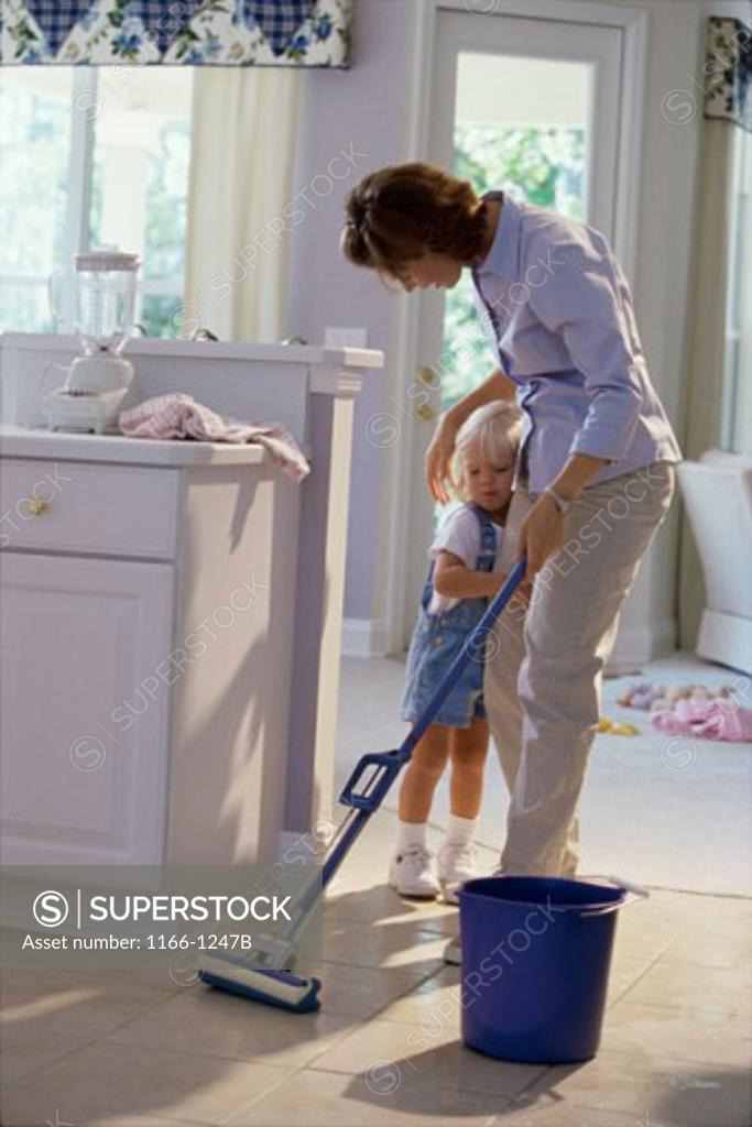 Stock Photo: 1166-1247B Mother cleaning the kitchen floor with her daughter standing beside her