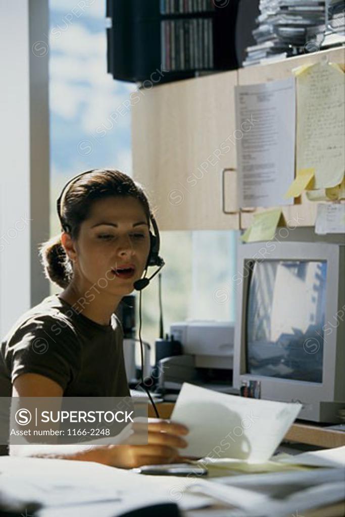 Stock Photo: 1166-2248 Female customer service representative wearing a headset and reading documents