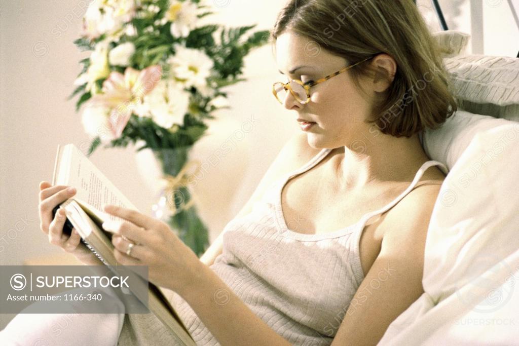 Stock Photo: 1166-340 Side profile of a young woman reading a book in bed