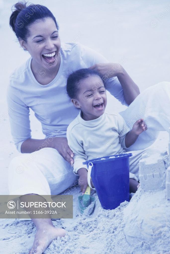 Stock Photo: 1166-3922A Young woman sitting on sand with her daughter