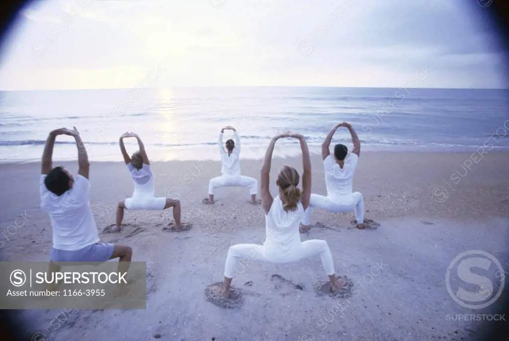 Rear view of a group of people performing yoga on the beach