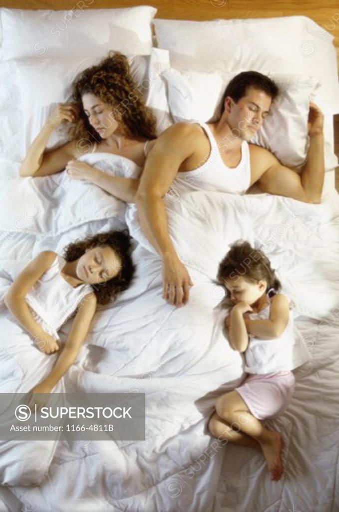 Stock Photo: 1166-4811B Mid adult couple sleeping with their son and daughter on a bed