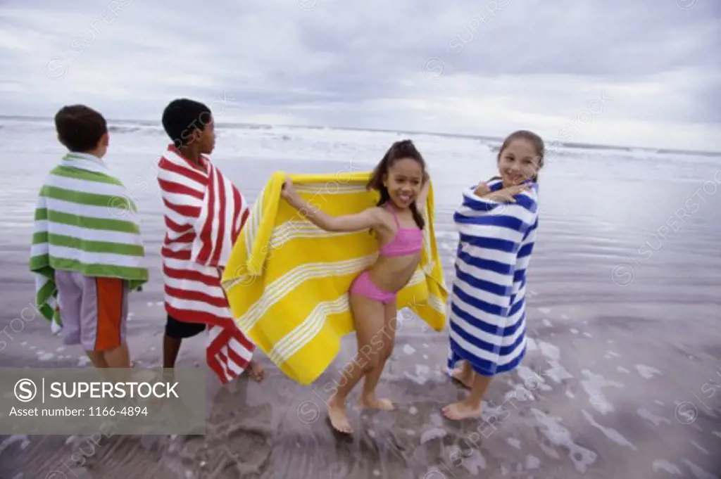 Two boys and two girls wrapped in towels on the beach