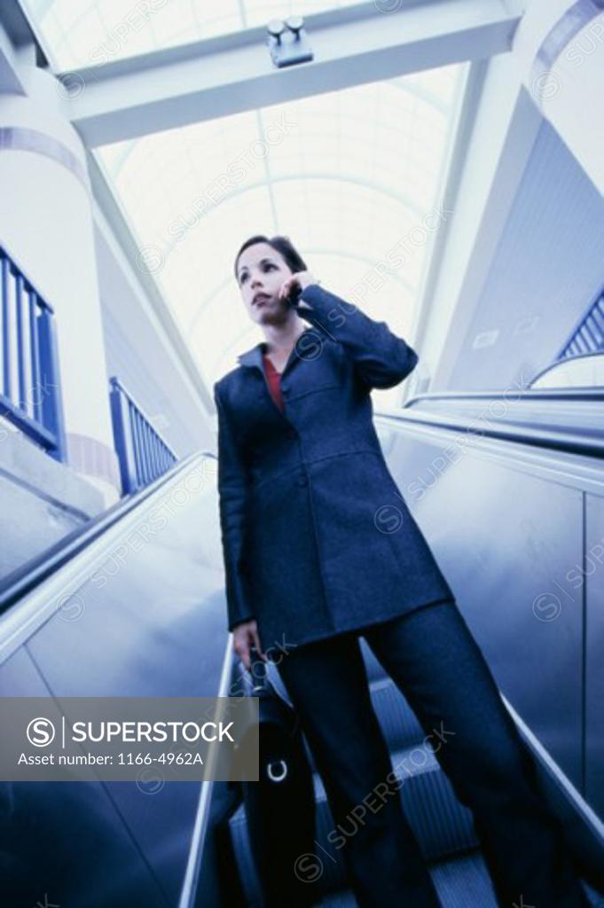 Stock Photo: 1166-4962A Low angle view of a businesswoman standing on an escalator talking on a mobile phone