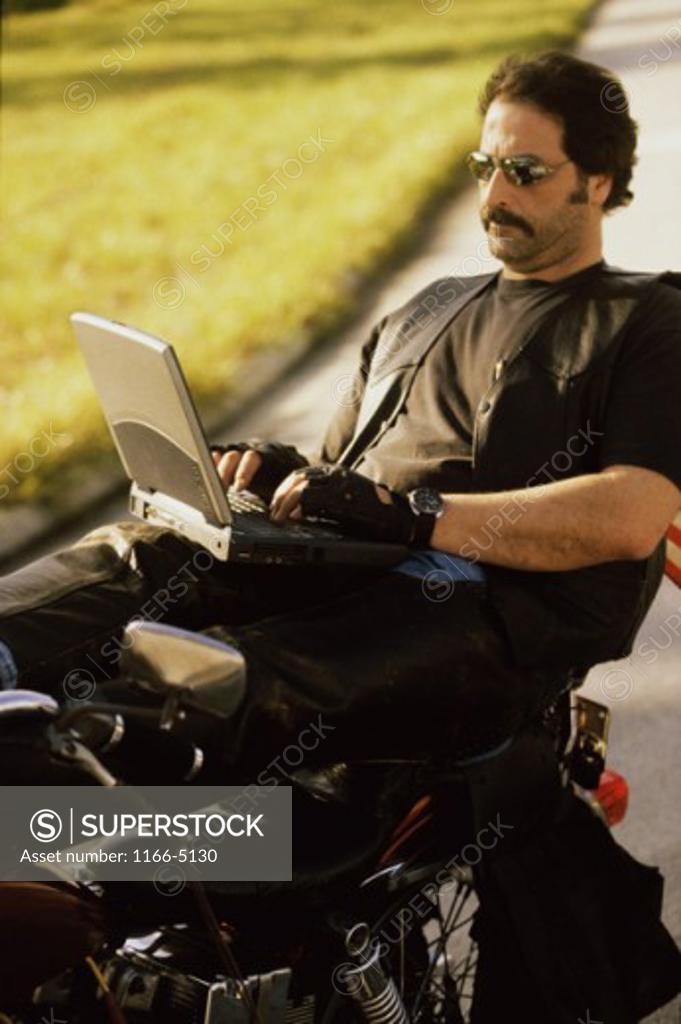 Stock Photo: 1166-5130 Mid adult man sitting on a motorcycle using a laptop