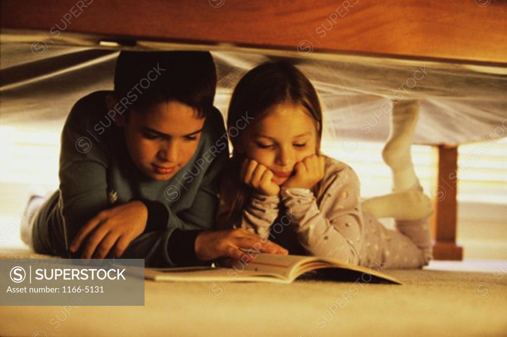 Stock Photo: 1166-5131 Boy and a girl reading a book under the bed
