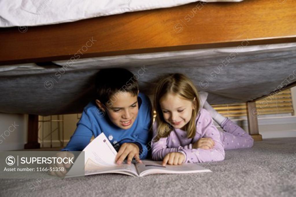 Stock Photo: 1166-5135B Boy and a girl reading a book under the bed