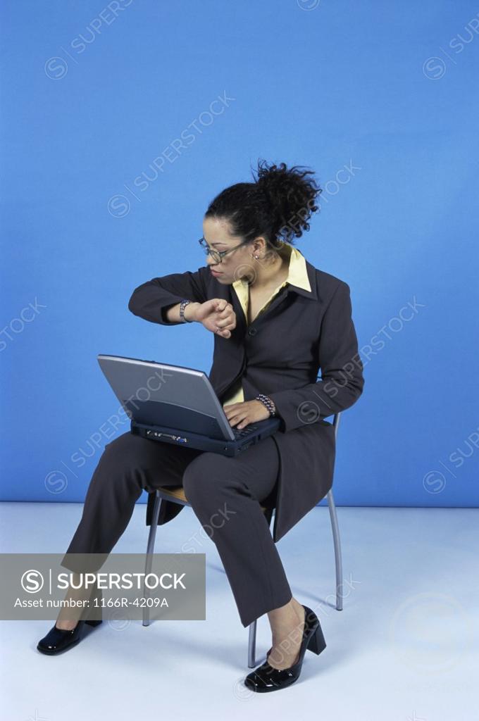 Stock Photo: 1166R-4209A Businesswoman sitting on a chair looking at her wristwatch while working on a laptop