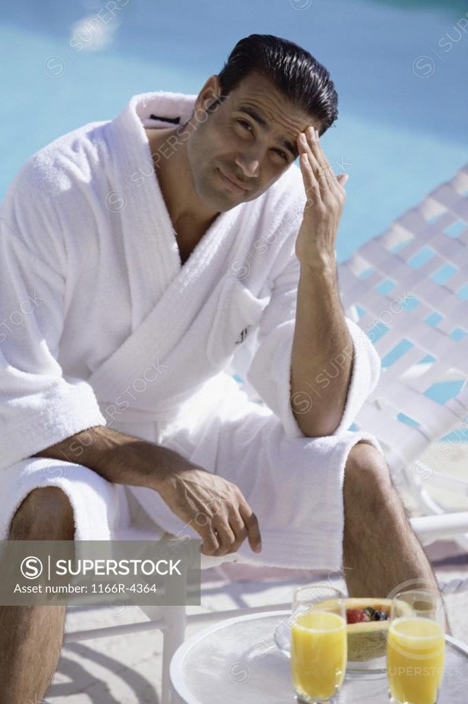 Stock Photo: 1166R-4364 Portrait of a young man sitting in a bathrobe at the poolside