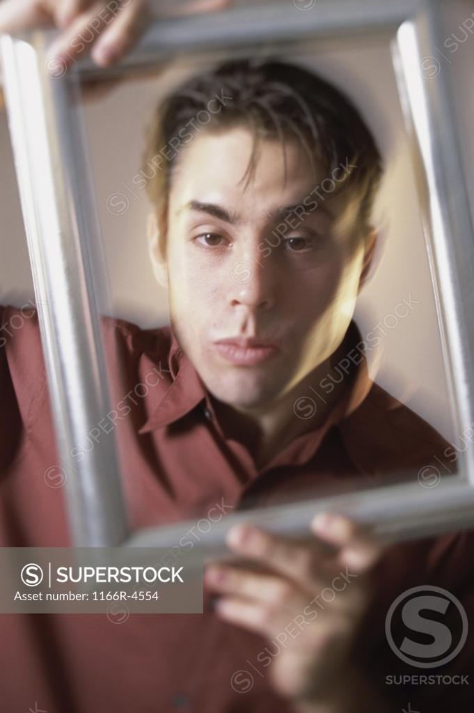Stock Photo: 1166R-4554 Portrait of a young man looking through a picture frame