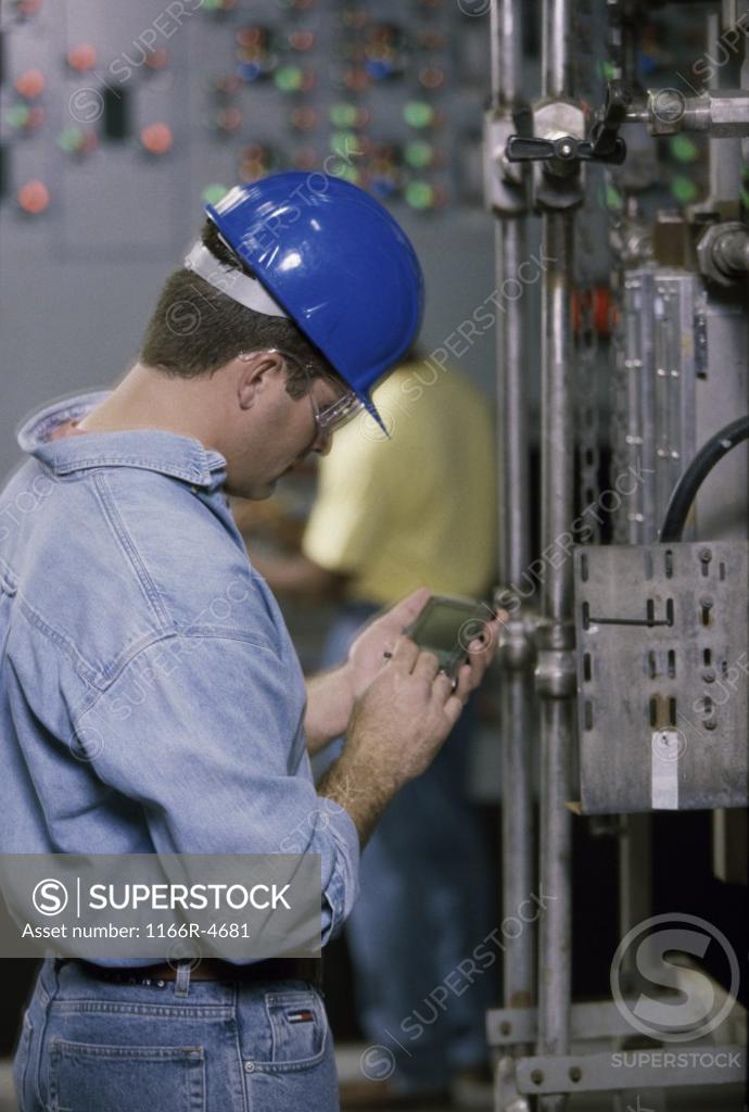 Stock Photo: 1166R-4681 Worker standing beside machinery at a power plant operating a hand held device