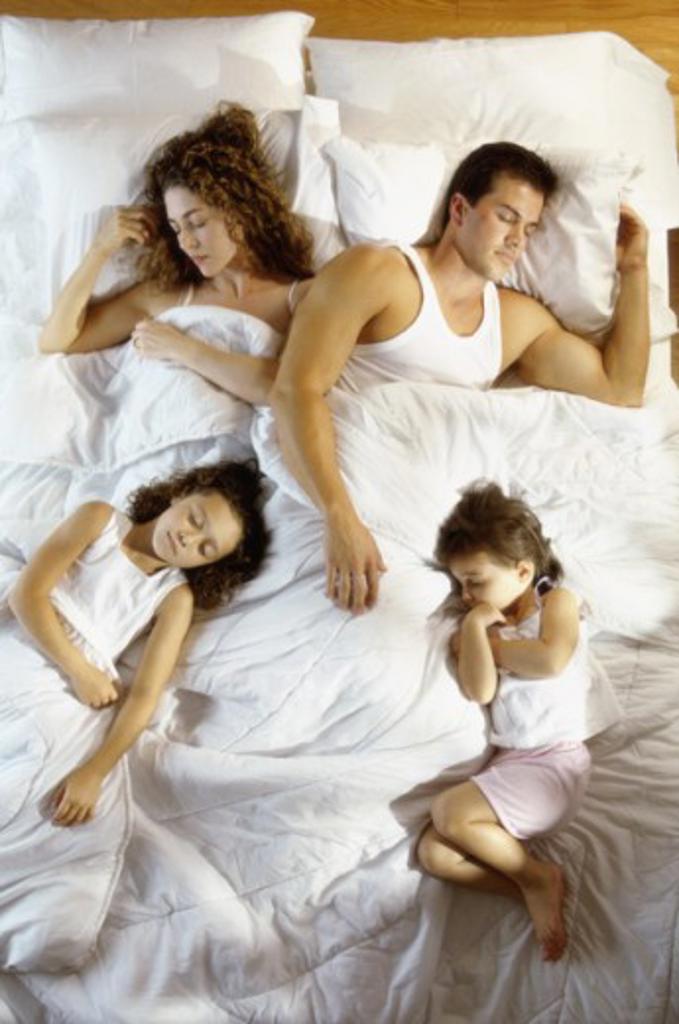 Mid adult couple sleeping with their son and daughter on a bed