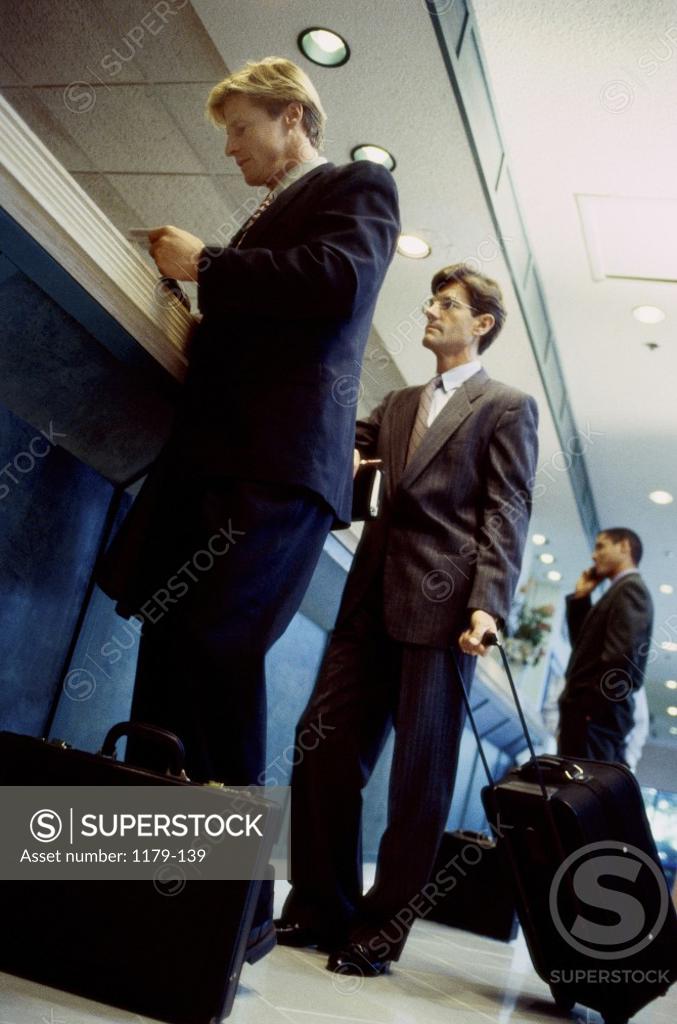 Stock Photo: 1179-139 Three businessmen standing at an airport check-in counter