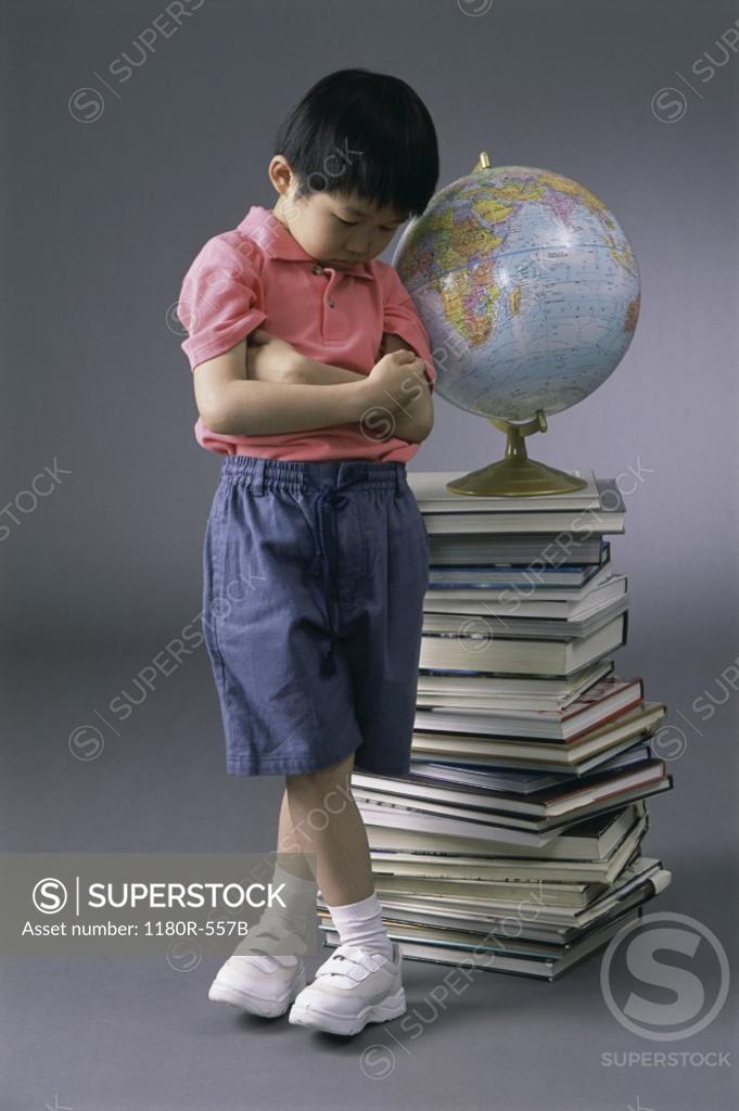 Stock Photo: 1180R-557B Boy standing near a pile of books and a globe