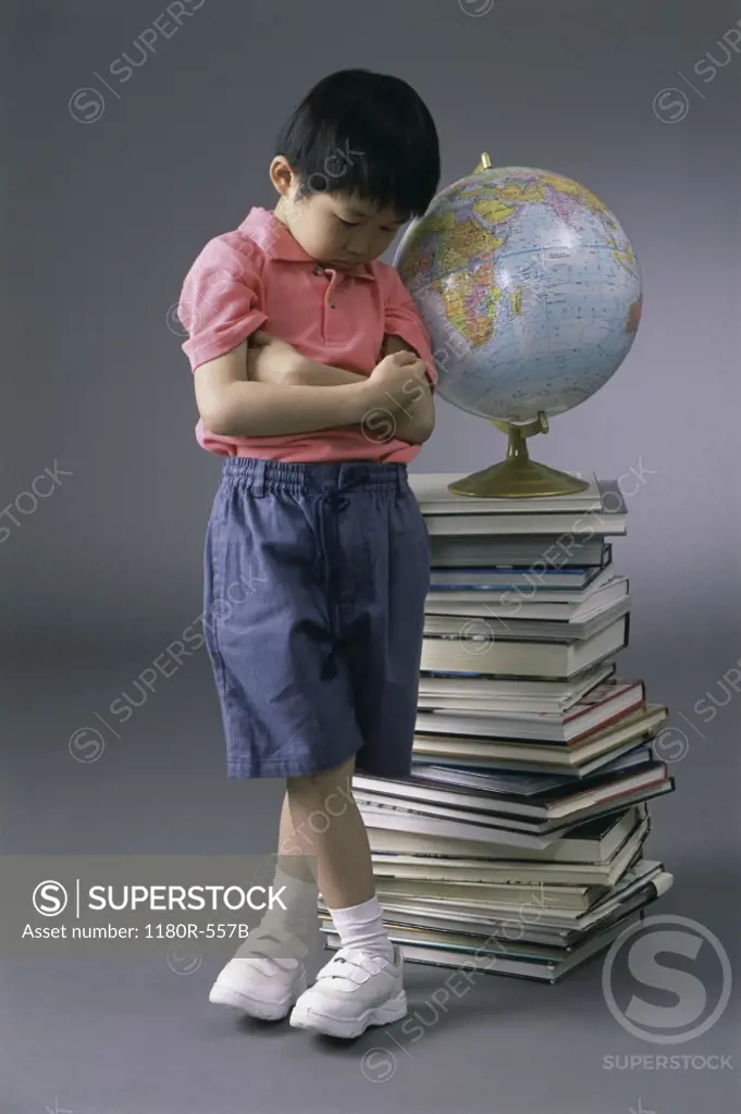 Boy standing near a pile of books and a globe
