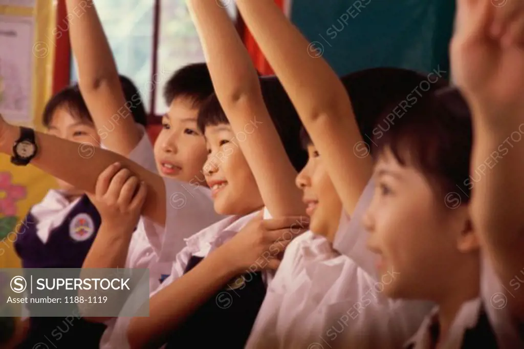 Group of children raising their hands in a row and smiling