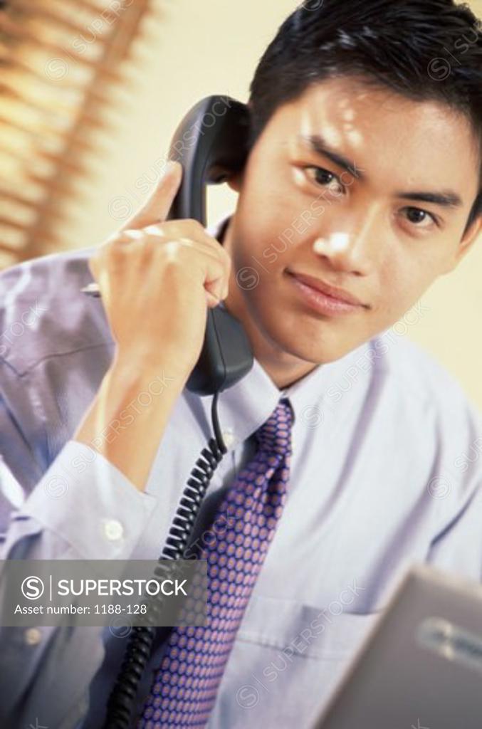 Stock Photo: 1188-128 Portrait of a young businessman using the landline telephone at his desk