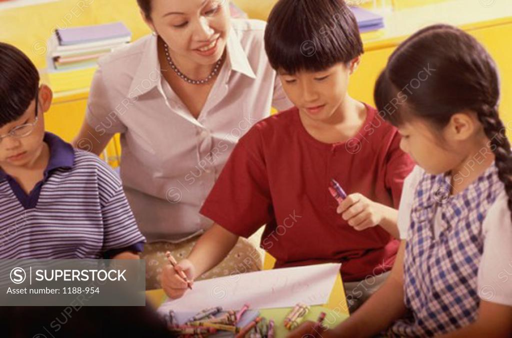 Stock Photo: 1188-954 Two boys and a girl coloring with crayons and their teacher looking at them