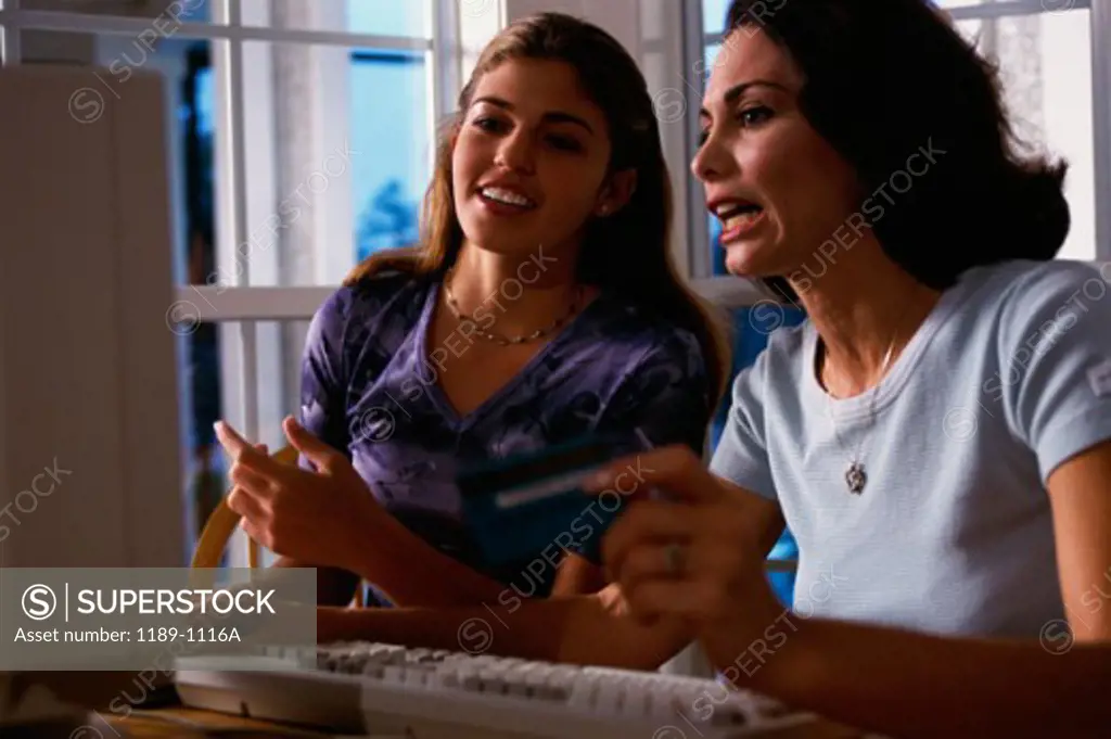 Mother with her daughter using a computer and holding a credit card