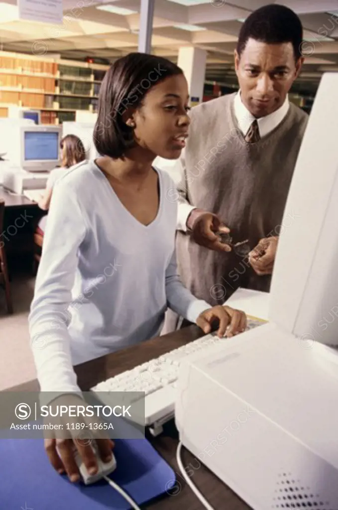 Male teacher and a teenage girl in front of a computer