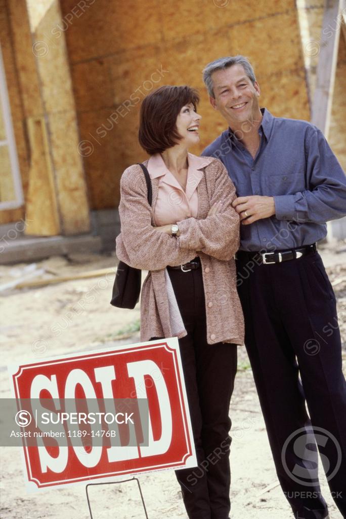 Stock Photo: 1189-1476B Mature couple standing in front of a house with a sold sign