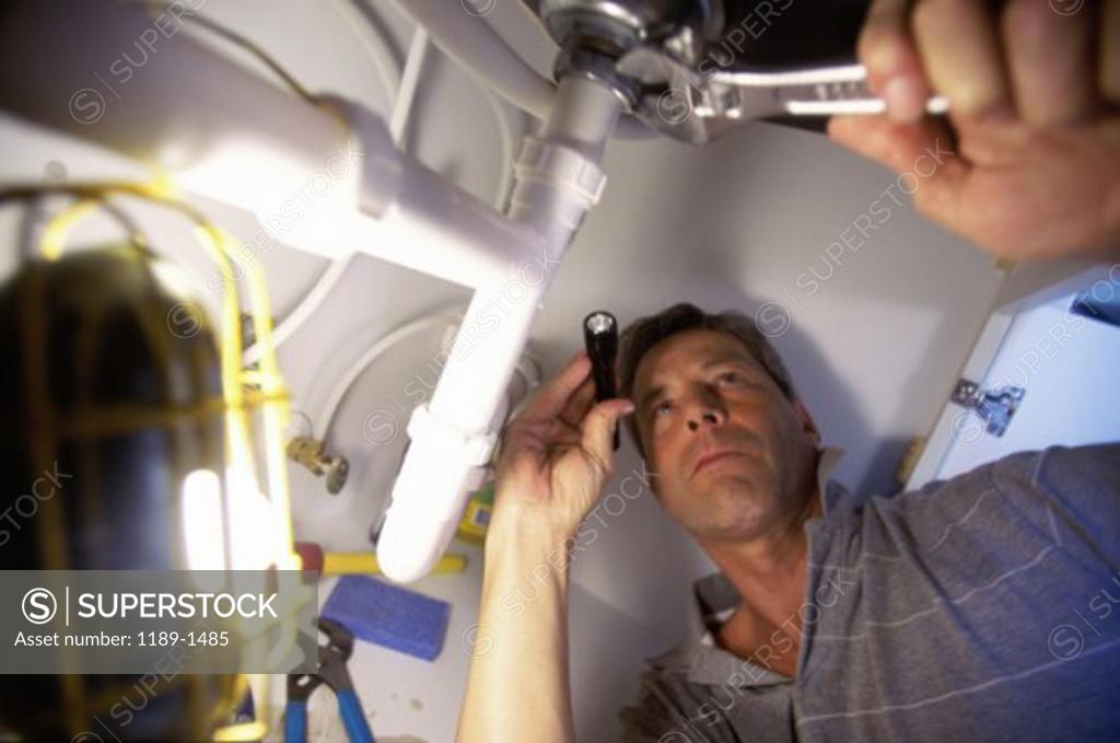 Stock Photo: 1189-1485 Low angle view of a young man checking the plumbing with a flashlight