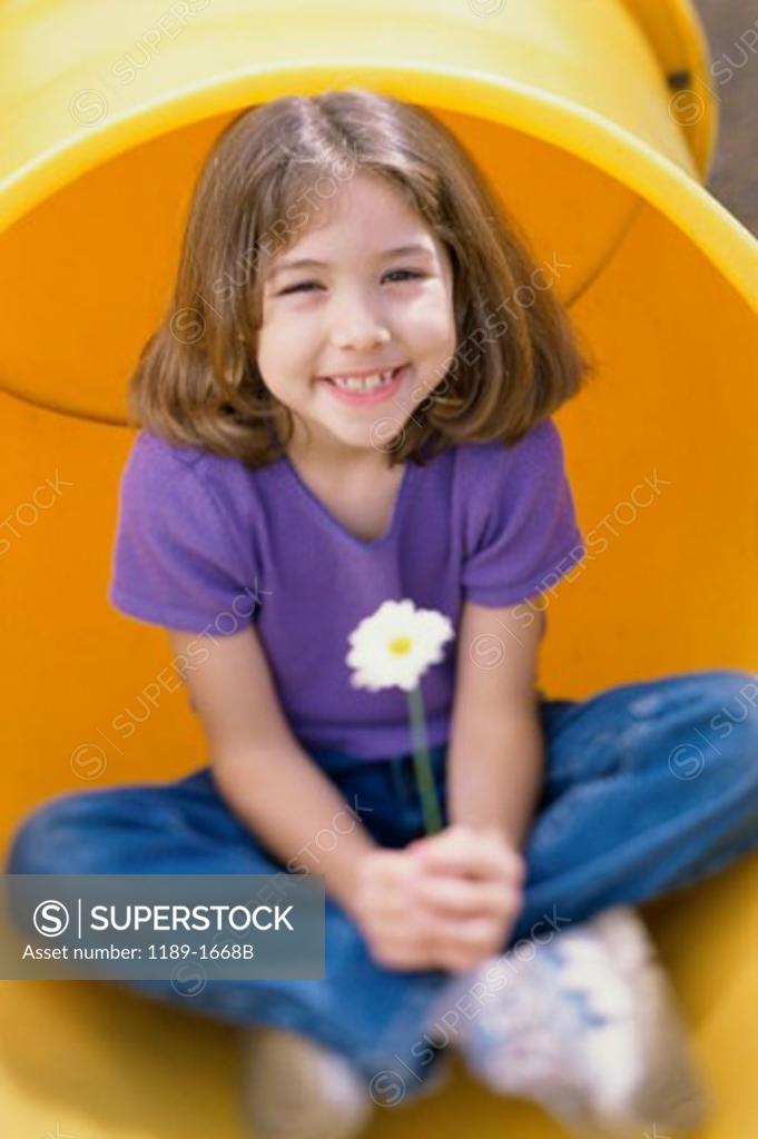 Stock Photo: 1189-1668B Girl sitting in a pipe and holding a daisy