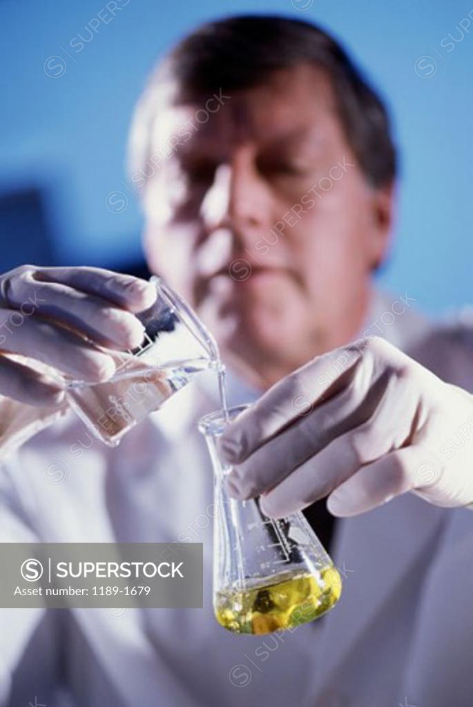 Stock Photo: 1189-1679 Male researcher pouring liquid from a measuring beaker into a conical flask