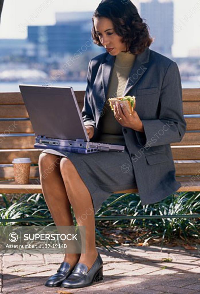 Stock Photo: 1189-1914B Businesswoman using a laptop and holding a sandwich