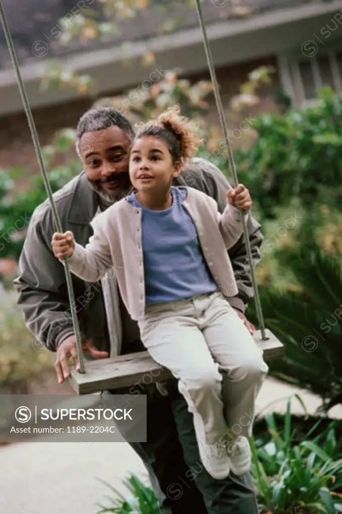 Senior man pushing his granddaughter on a swing