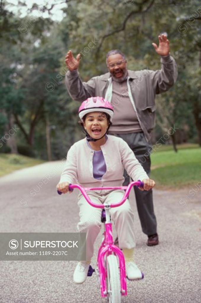 Stock Photo: 1189-2207C Girl riding a bicycle with her grandfather standing behind her